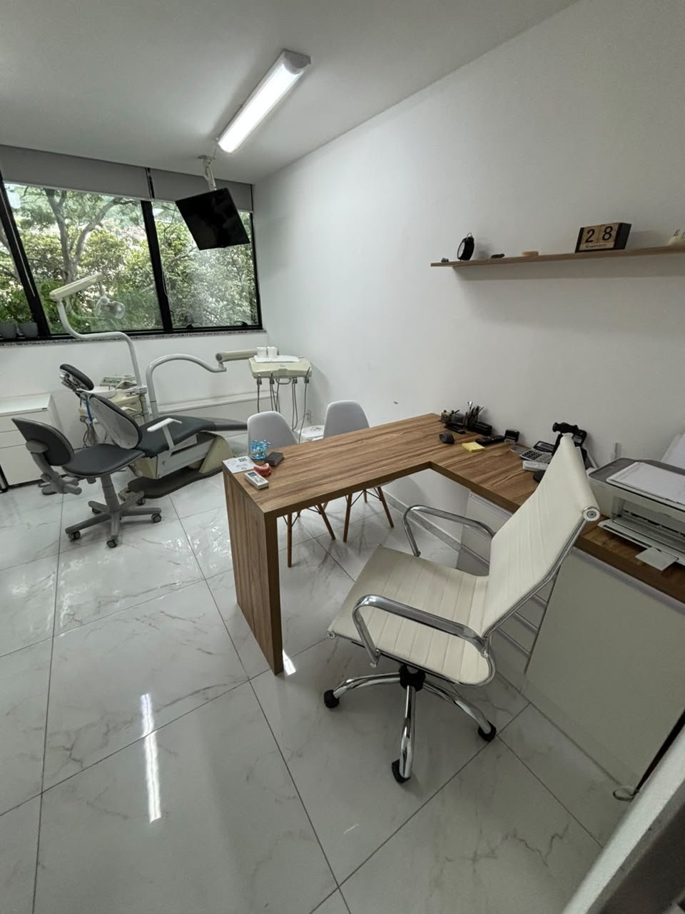 Sala de atendimento com mesa de consulta, cadeira odontológica e janela para a rua